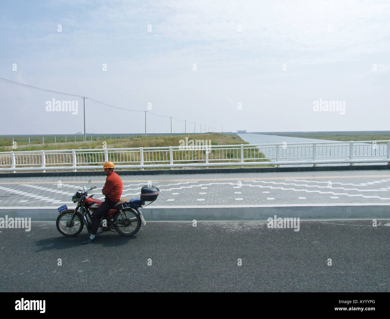 Ein Mann auf einem Motorrad vor dem Kanal verbinden Wasser Tropfen See mit dem Meer Lingang New Town in der Nähe von Shanghai China Stockfoto