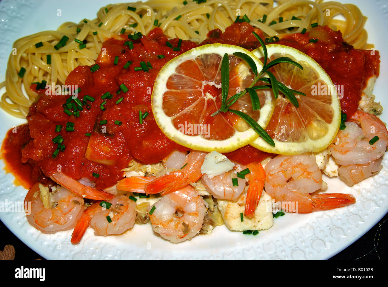 Fischgericht Linguine mit Garnelen, Heilbutt und Muscheln in einer reichhaltigen Tomatensauce mit Zitrone, Knoblauch, Zwiebeln, Schnittlauch und Frühlingszwiebeln. Stockfoto