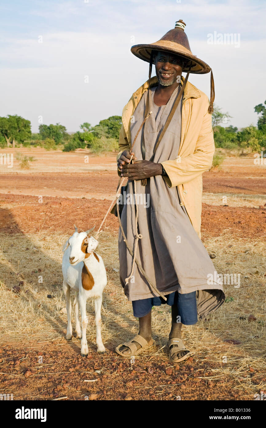 Mali, Mopti. Ein Fulani-Mann einen traditionellen Hut nimmt nach Hause eine Ziege, die er in einen Wochenmarkt gekauft. Stockfoto