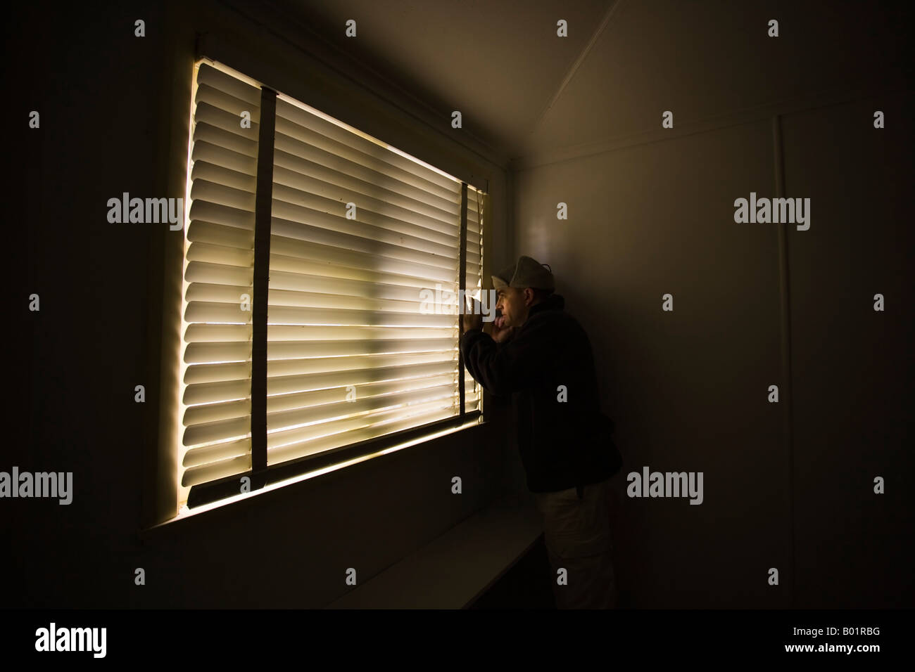 Vierzig Mann schaut aus Fenster durch Lamellen der Jalousie Stockfoto