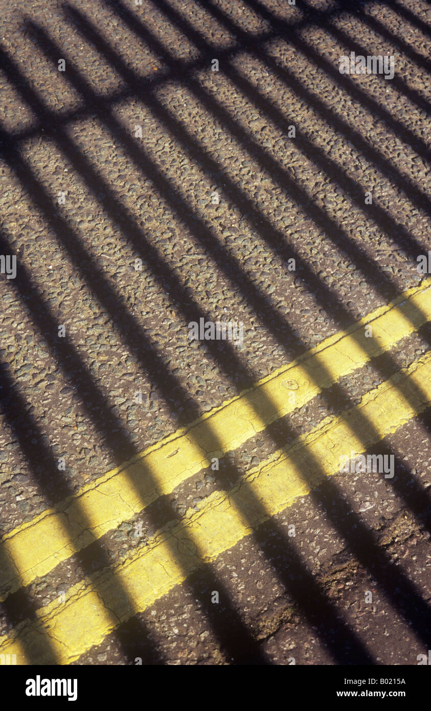 Der Metallzaun Geländer Schatten über asphaltierte Straße mit doppelten gelben Linien keine Parkplätze Stockfoto