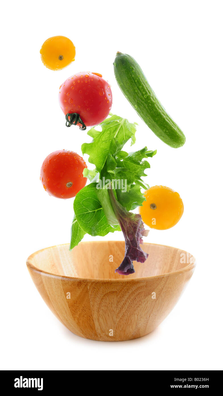 Verschiedene frische Gemüse, die fallen in eine hölzerne Salatschüssel isoliert auf weißem Hintergrund Stockfoto