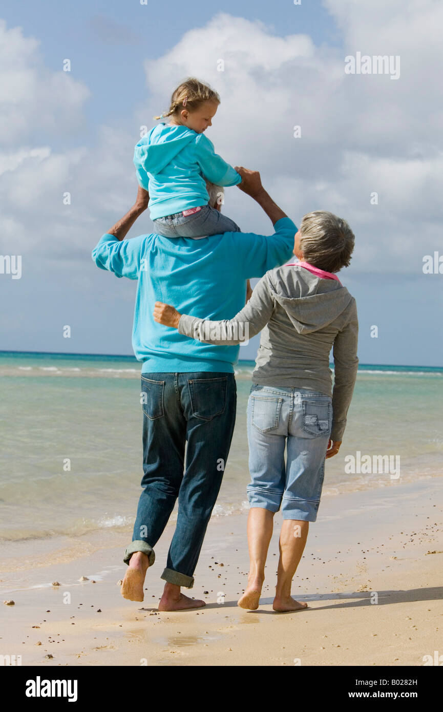Rückansicht der Großeltern Strand entlang spazieren, mit Großvater tragen junge Mädchen piggback Stockfoto