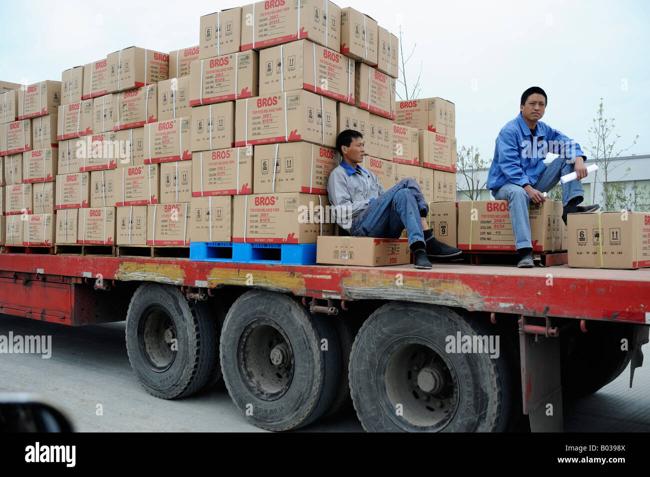 Zwei chinesische Arbeiter auf einem Plattformwagen convoying gefärbt Melange-Garn in Ningbo, Zhejiang Provinz, China 19. April 2008 Stockfoto