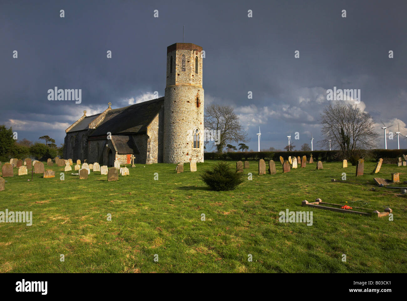 Kirche in Winterton am Meer mit der modernen Windkraftanlagen in der Ferne an einem stürmischen Tag auf dem Lande in Norfolk. Stockfoto