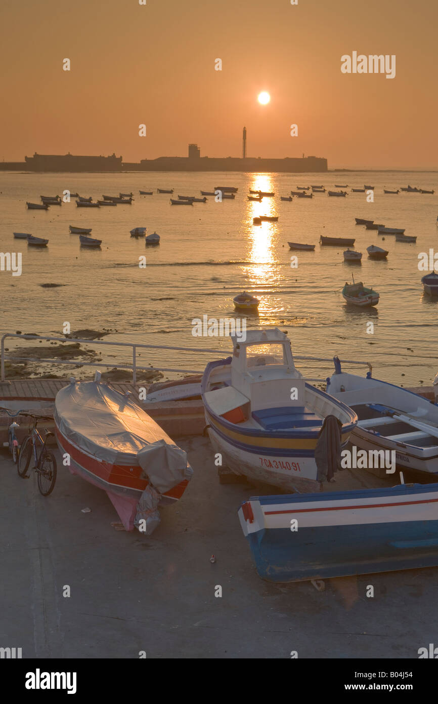 Kleine Fischerboote am Playa De La Caleta Backdropped von Castillo de San Sebastian bei Sonnenuntergang in der Stadt Cadiz Stockfoto