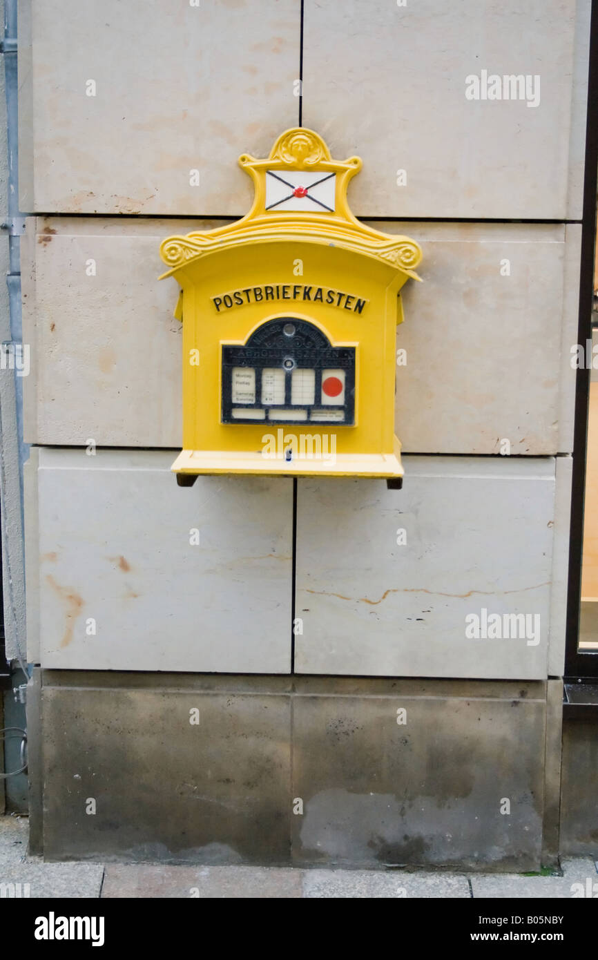 Vintage-gelber Postbriefkasten auf einer beigefarbenen Steinmauer in Deutschland, mit klassischem deutschem Postdesign. Stockfoto
