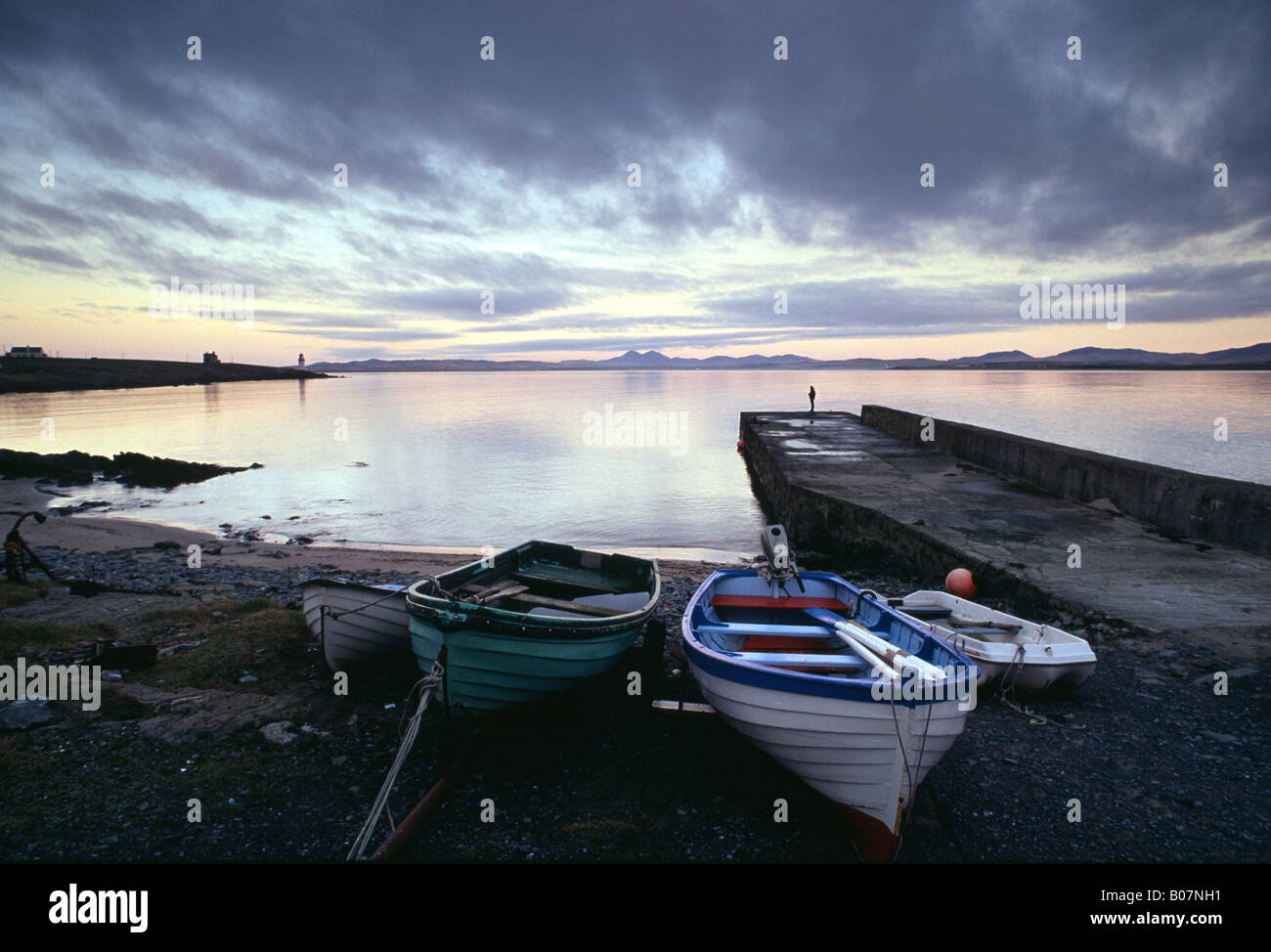 Abendlicht am Wasser und Boote Figur stehend an einem Anlegesteg Loch Indaal Islay Schottland Stockfoto