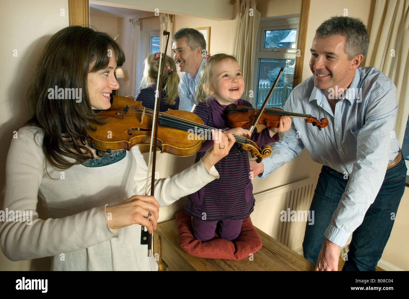 Eine Mutter und ihre kleine Tochter üben die Geige wie ein stolzer Vater blickt auf Stockfoto
