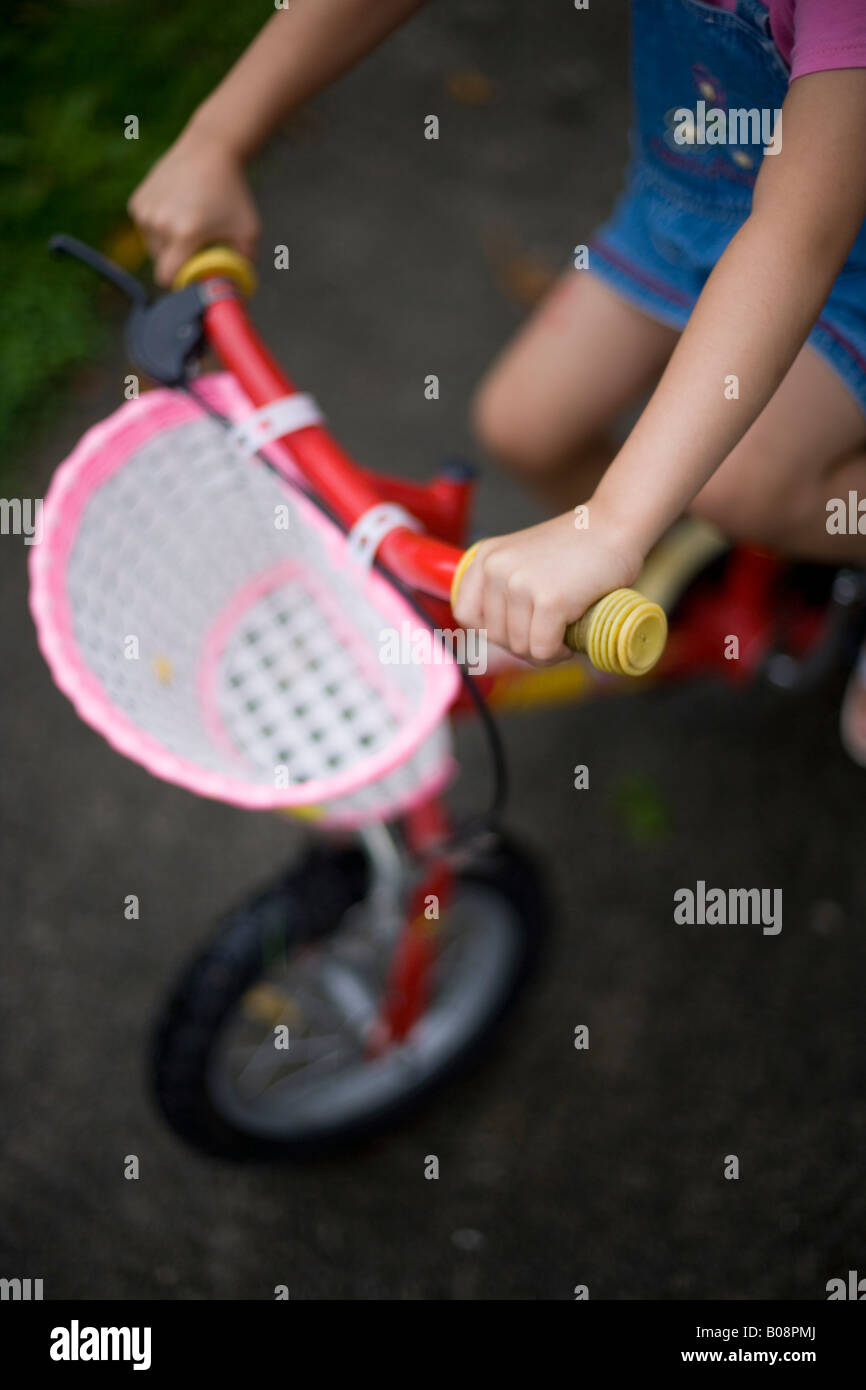 Mädchen im Alter von vier Fahrten Fahrrad mit Stützrädern und Korb rund um den Garten an einem verregneten Tag Stockfoto
