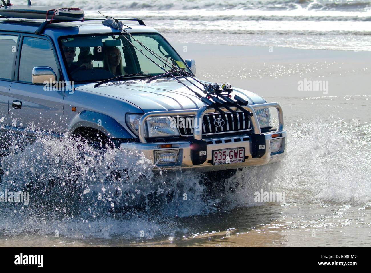 Toyota 4WD SUV mit Angelruten und Surfbrett montiert auf Motorhaube und Dach, die Fahrt durch das Spritzwasser am Strand, müssen Stockfoto