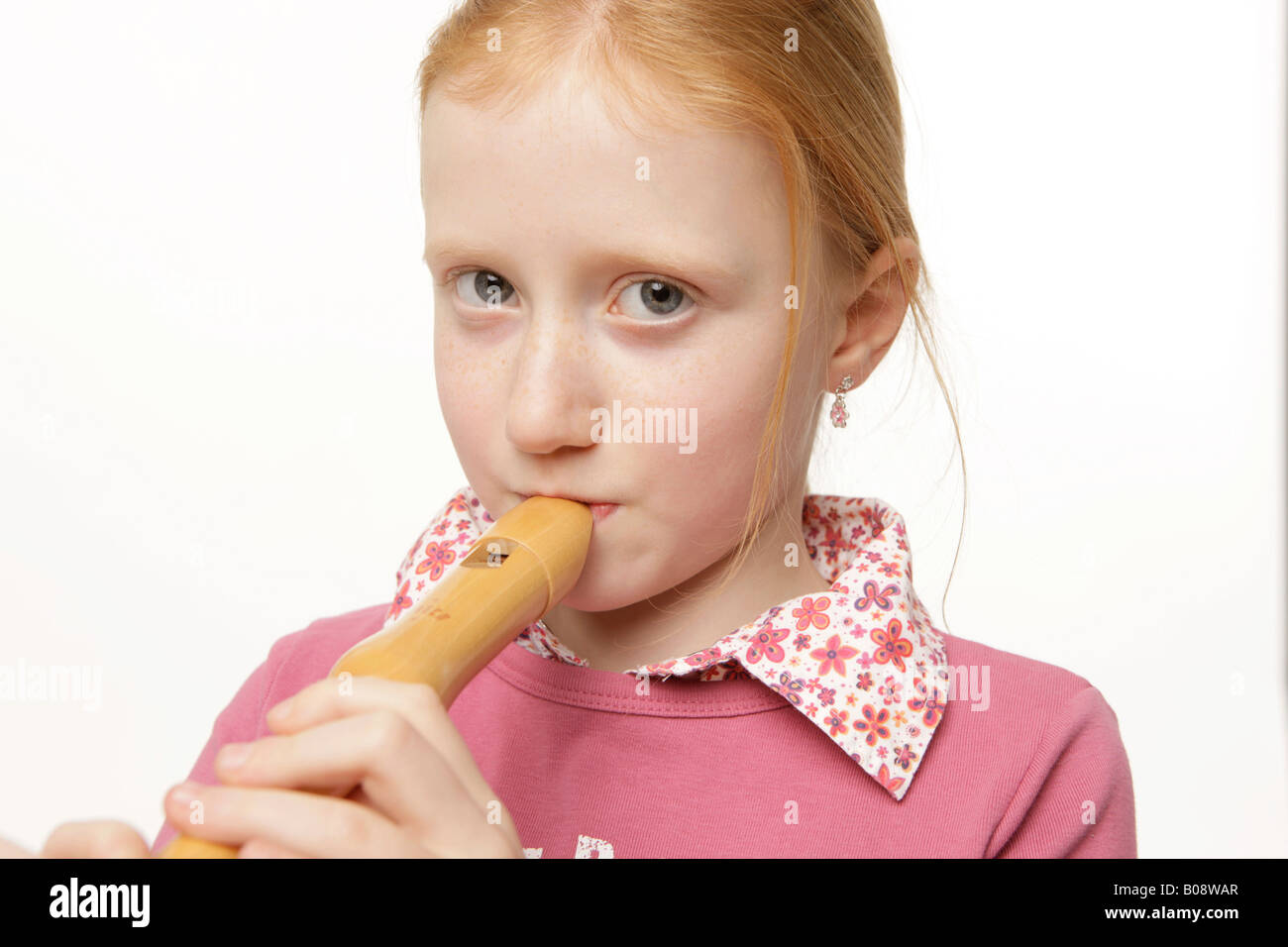 8 Jahre altes Mädchen mit roten Haaren spielt des Recorders Stockfoto