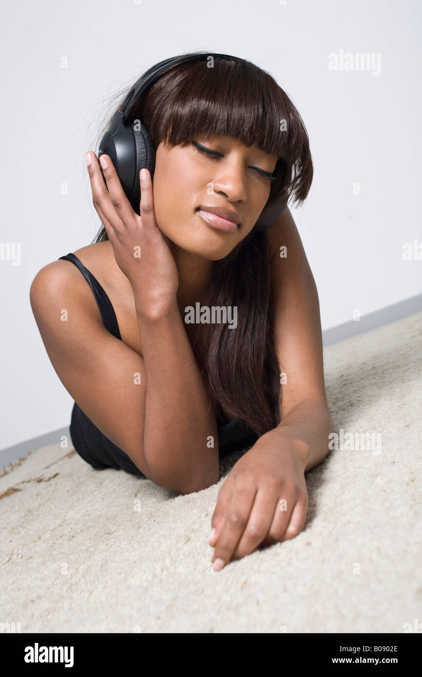 Junge, dunkelhäutige Frau liegend auf einem hellen Teppich Musikhören mit Kopfhörer Stockfoto