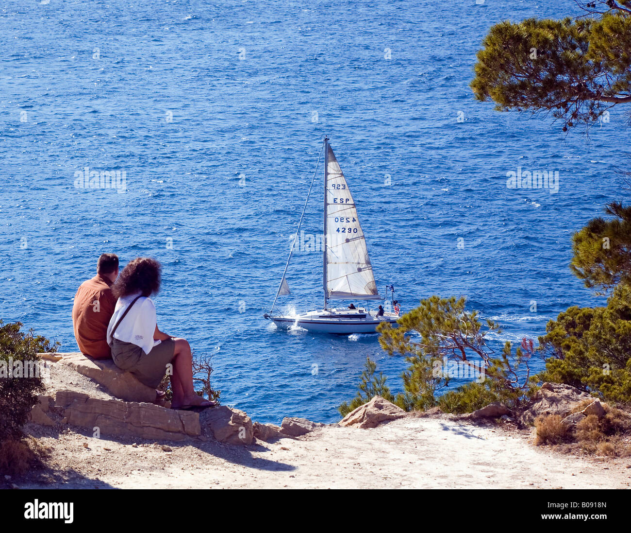 Paar sitzt am Rande einer Steilküste beobachten ein Segelboot in der Nähe von Sant Elm, Mallorca, Balearen, Spanien Stockfoto