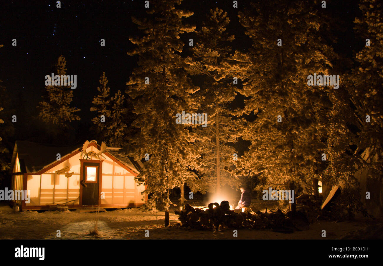 Beleuchtete Hütte, Elch Geweih montiert über der Tür, Lagerfeuer in einem Wald im Winter, Yukon Territorium, Kanada Stockfoto