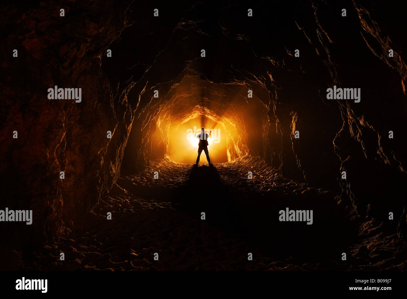 Ein Mann steht Höhenplan am Ende einer dunklen Höhle wie Tunnel wo gibt es ein helles Licht, das hinter ihm. Stockfoto