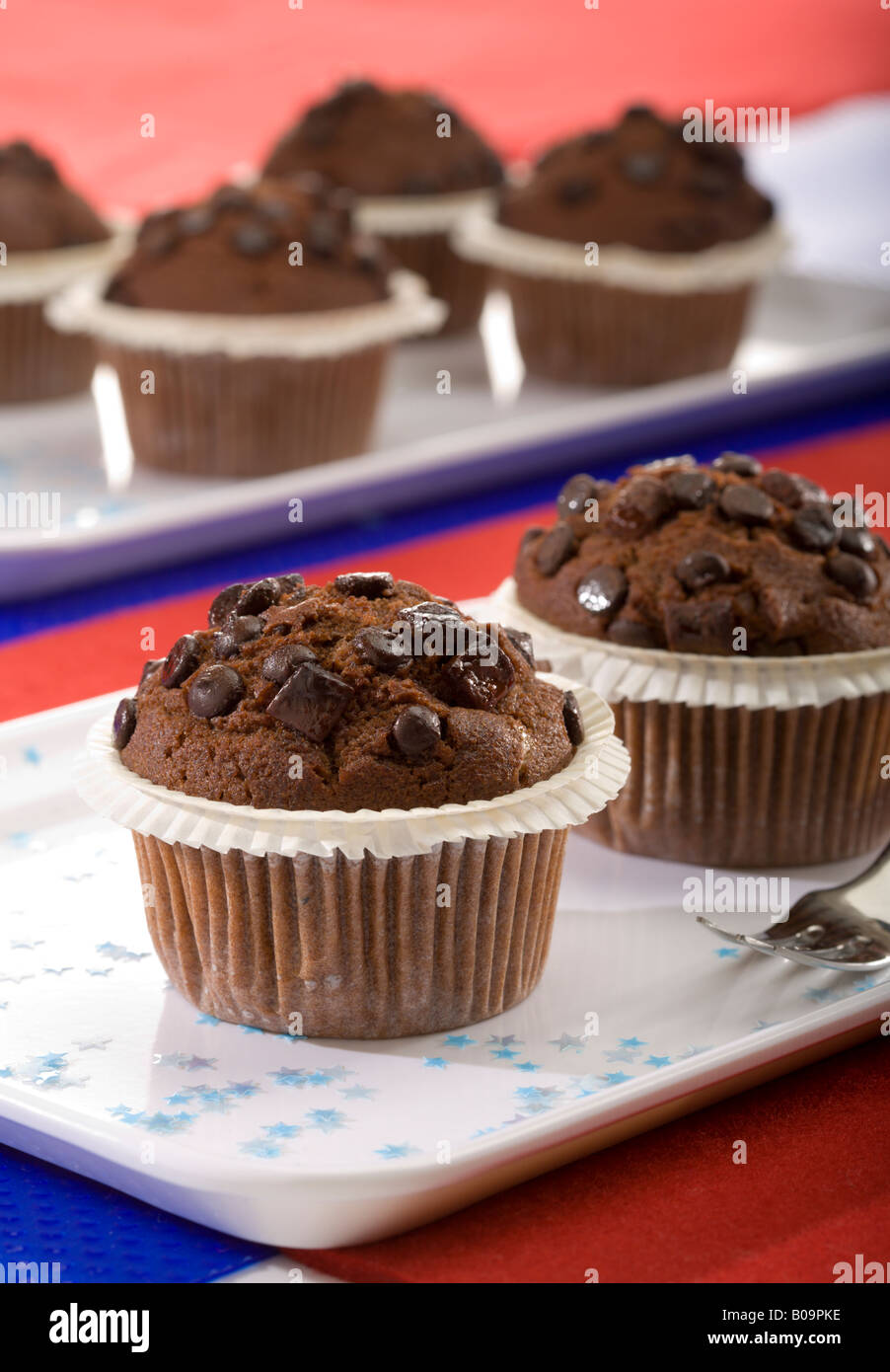Schokoladen-Muffins auf weißen Platten, verziert mit kleinen Sternen auf blauem und rotem Hintergrund Stockfoto