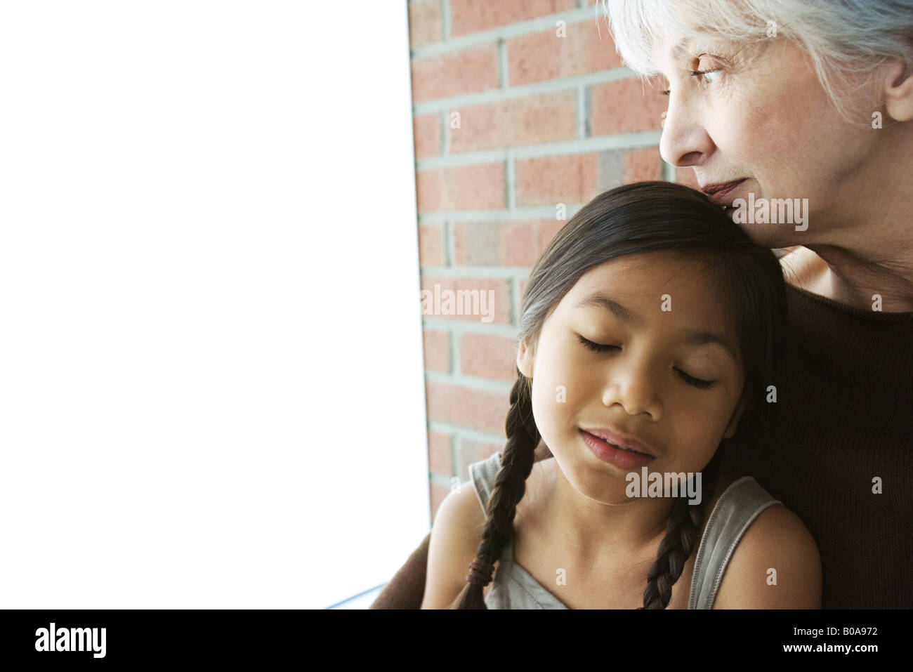 Ältere Frau ruht ihr Kinn auf Enkelin Kopf, Augen des Mädchens geschlossen Stockfoto