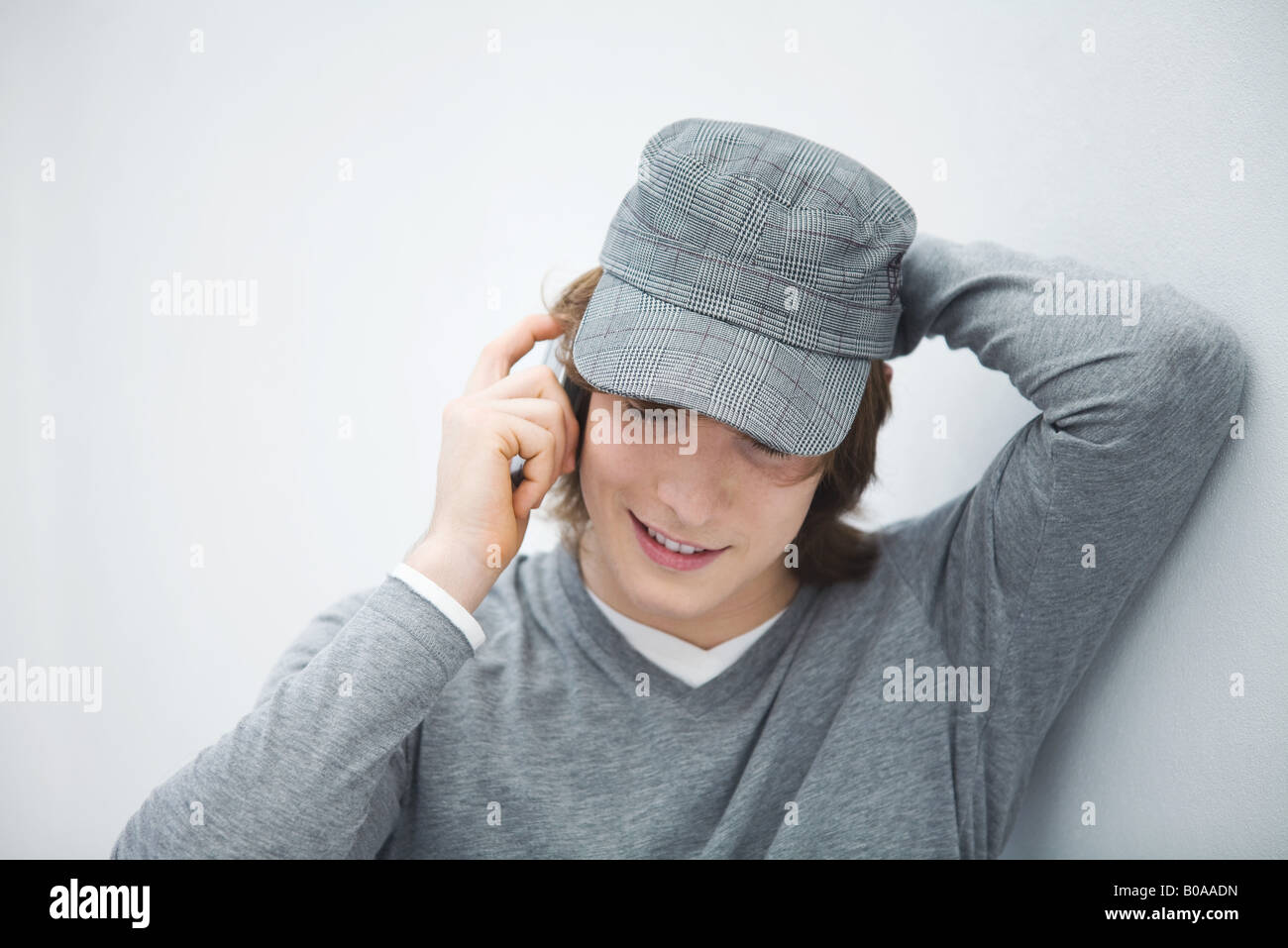 Junger Mann in Kappe mit Handy, Blick nach unten, eine Hand hinter den Kopf Stockfoto