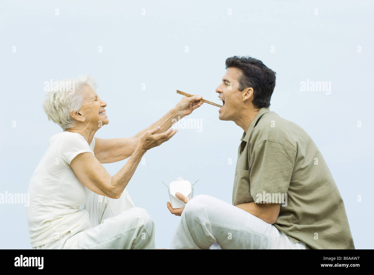 Ältere Frau Fütterung erwachsenen Sohn mit Stäbchen, lachen, Seitenansicht Stockfoto