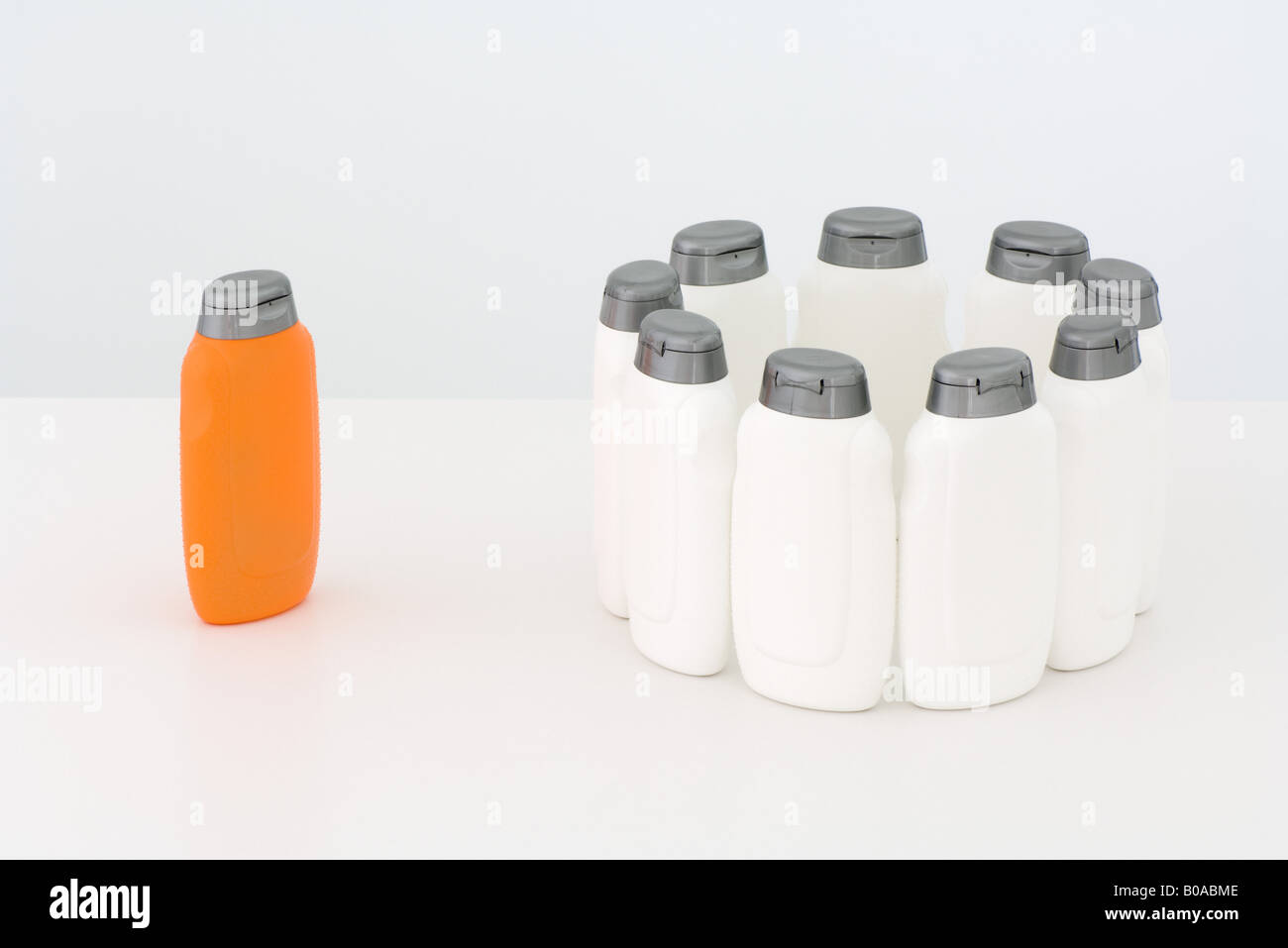 Gruppe von weißen Flaschen im Kreis und einzelne orange Flasche Stockfoto