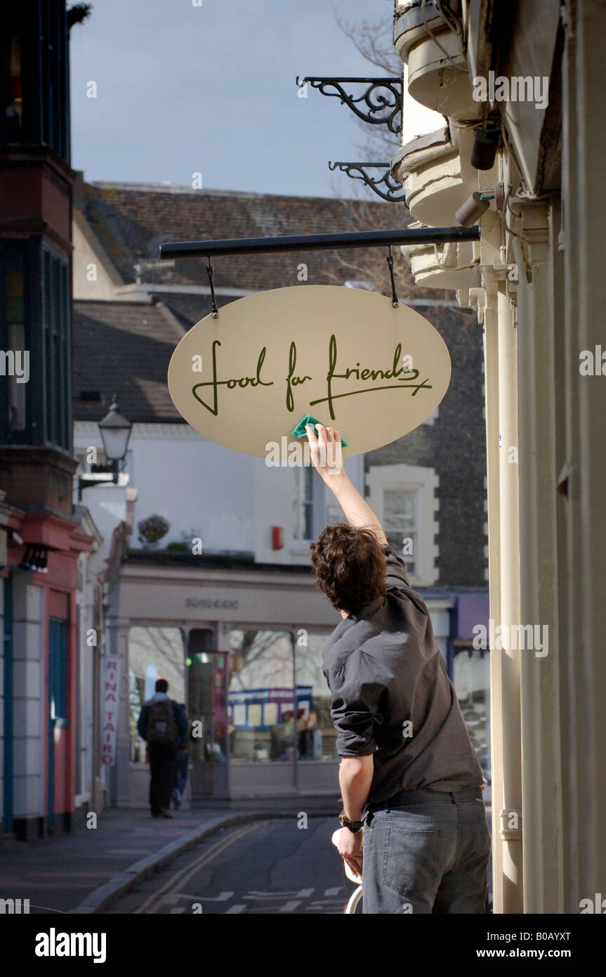 Ein Mitarbeiter reinigt das Schild im Restaurant „Food for Friends“ im Stadtteil Lanes von Brighton, East Sussex, Großbritannien. Nur für redaktionelle Zwecke Stockfoto