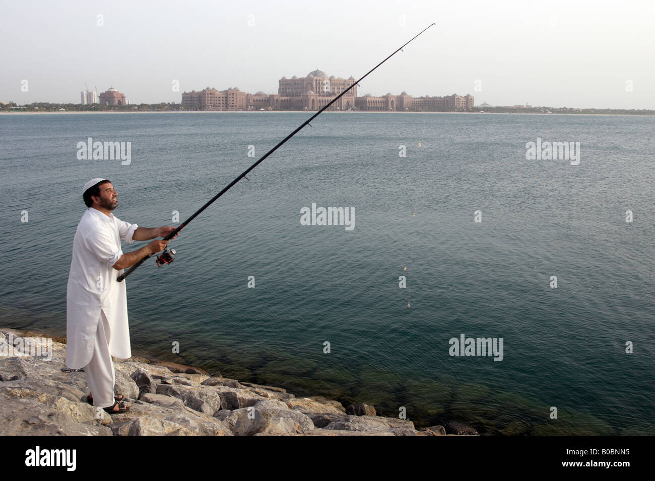 Ein Mann Angeln, das Emirates Palace Hotel im Hintergrund, Abu Dhabi, Vereinigte Arabische Emirate Stockfoto