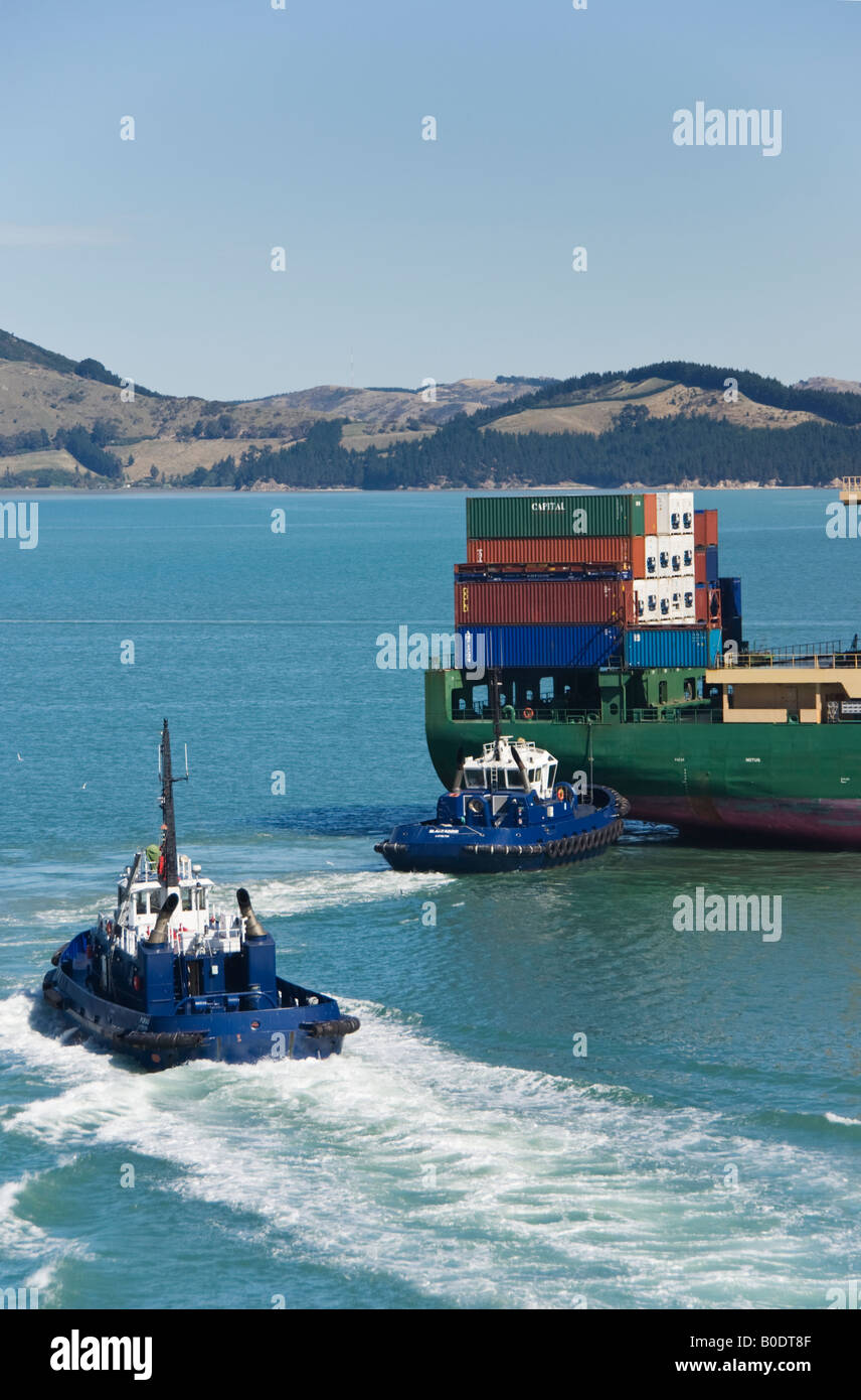 Ein Schlepper schiebt am Heck eines Containerschiffs, während andere sich auch Assist ankommt. Stockfoto