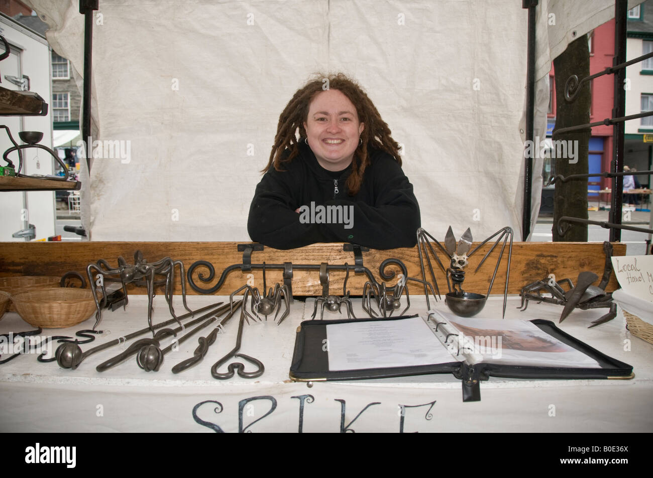 Junge Frau Stall Inhaber verkaufen Hand gemacht Schmiedeeisen Haushalt Geräte Machynlleth Markt Powys Wales UK Stockfoto