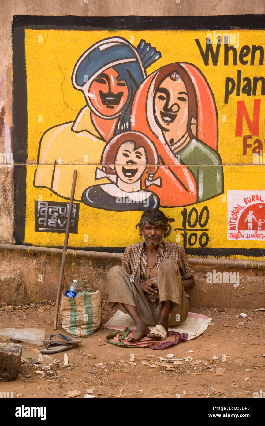 Ein Mann sitzt neben einer Anzeige, die den Wert der Familienplanung in der Stadt Panaji, Goa, Indien lobt. Stockfoto