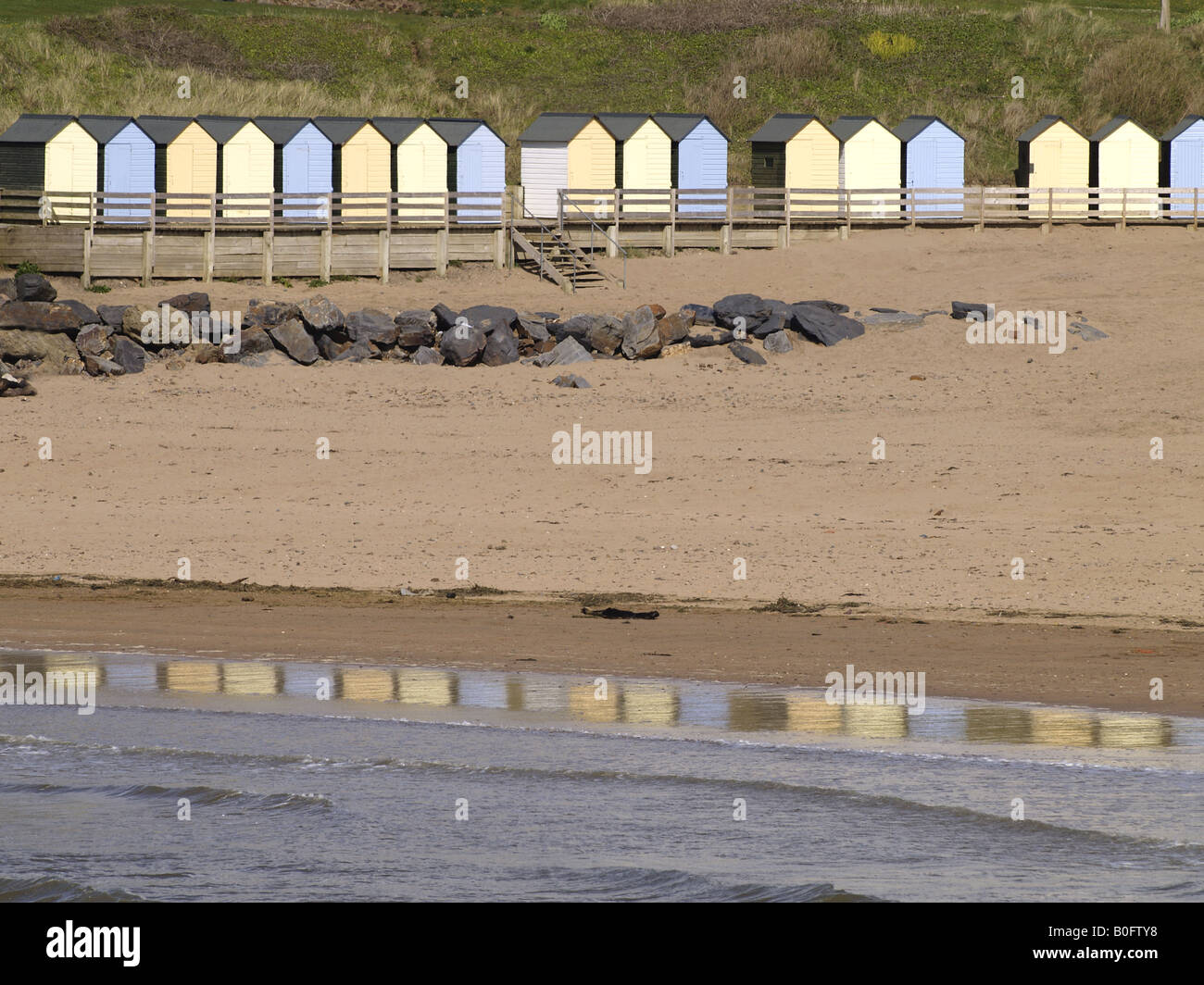 Eine Reihe von Strandhütten und ihre Reflexion in den Rand des Meeres, auf Summerleaze Beach, Bude, Cornwall, UK Stockfoto