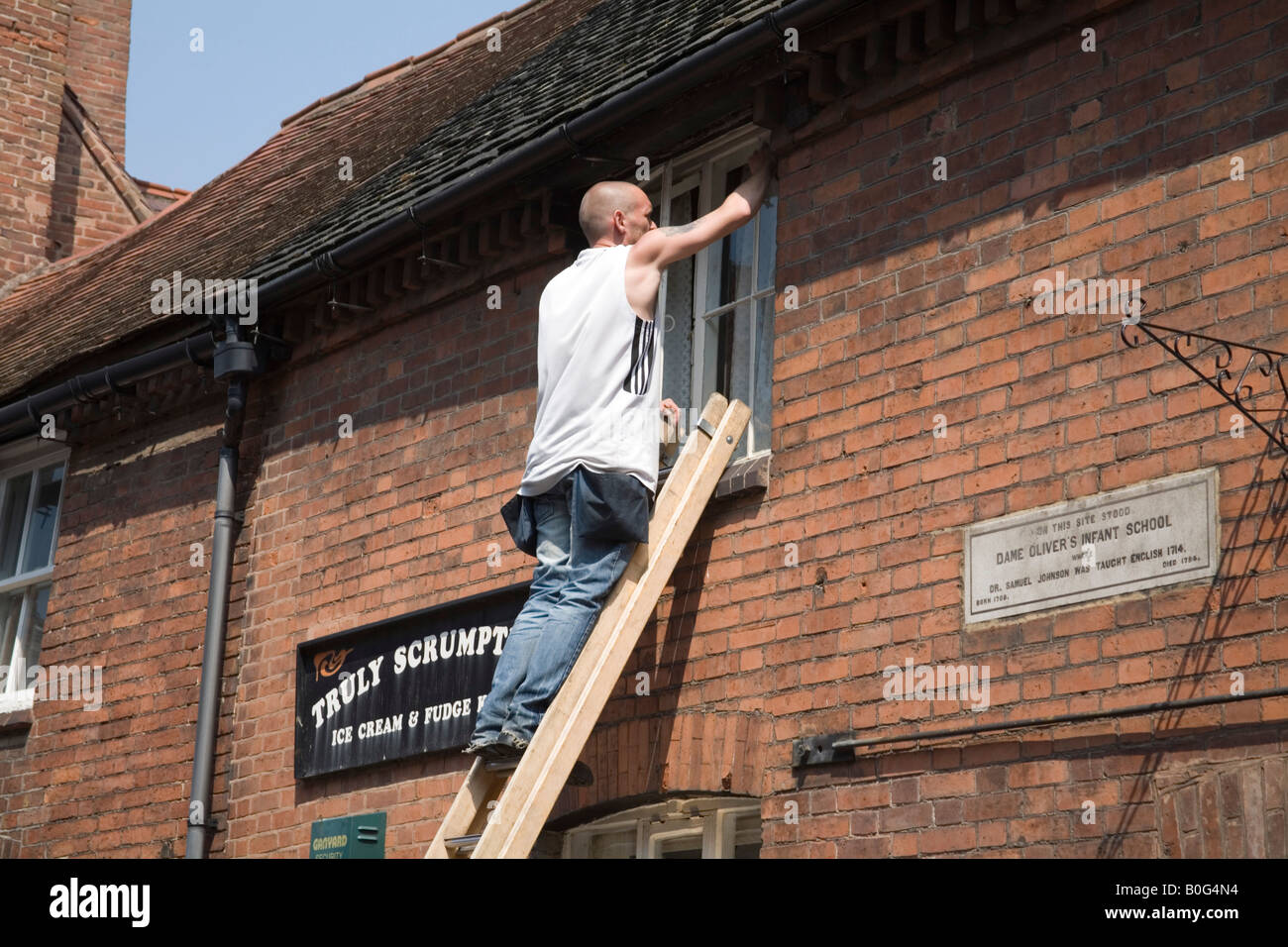 Staffordshire UK können männliche Fensterreiniger balancieren auf einer Leiter, die Reinigung der Frontscheiben der historischen Gebäude Stockfoto
