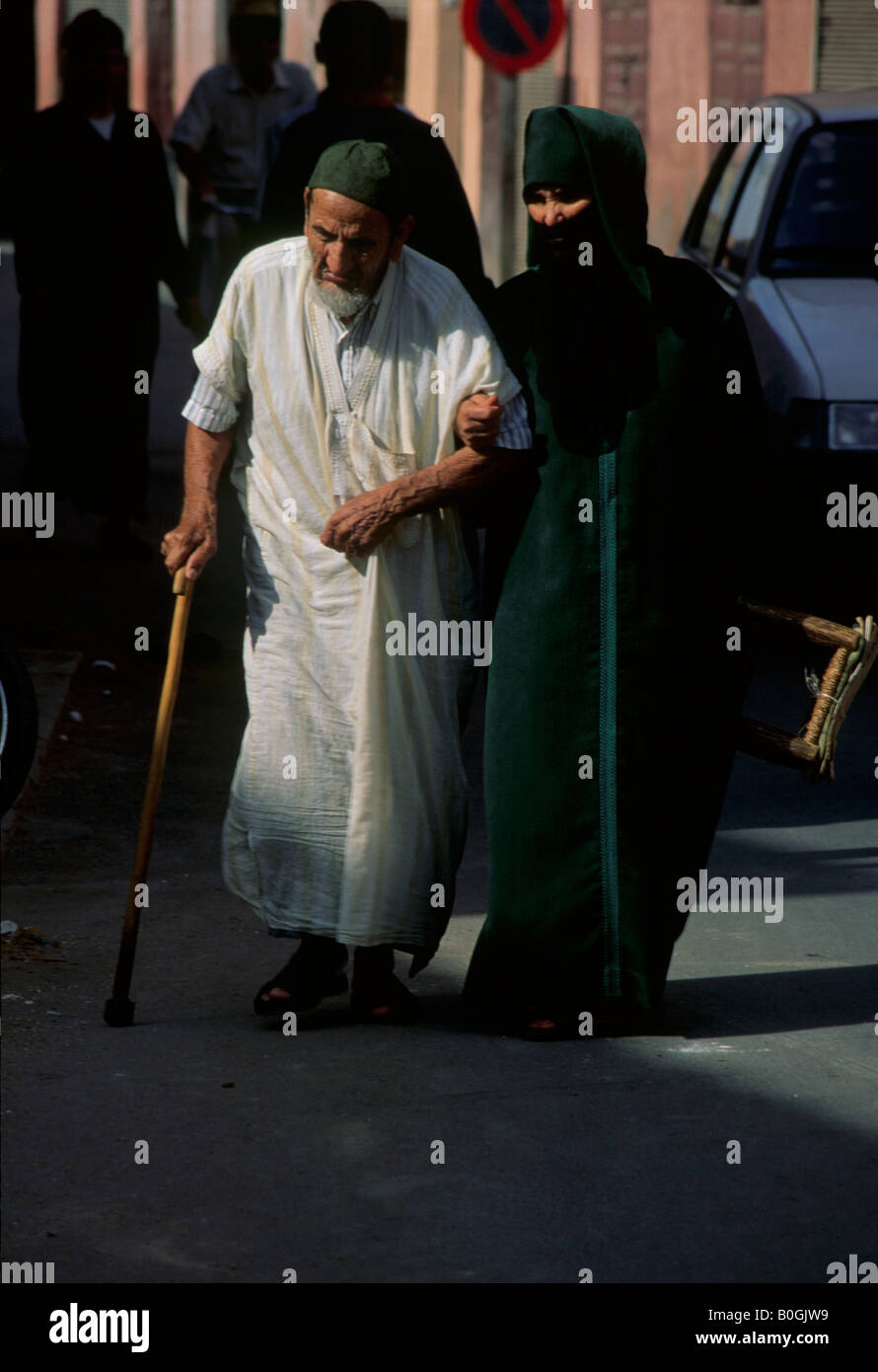 Eine verschleierte Frau hilft einen älteren Mann auf der Straße, Marrakesch, Marokko. Stockfoto