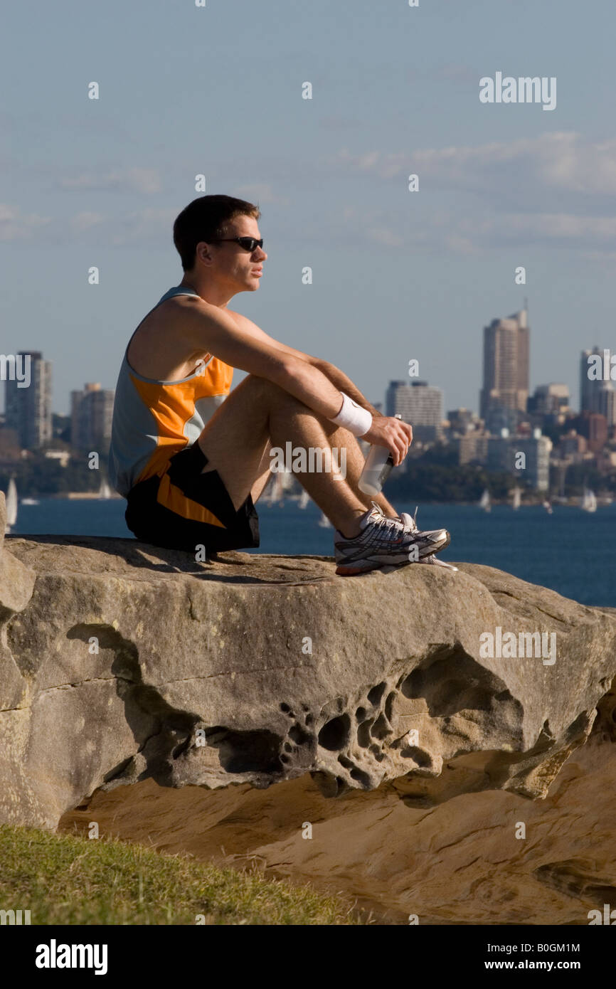 Männliche Läufer auf Felsen mit Blick auf Sydney hinter sitzen Stockfoto