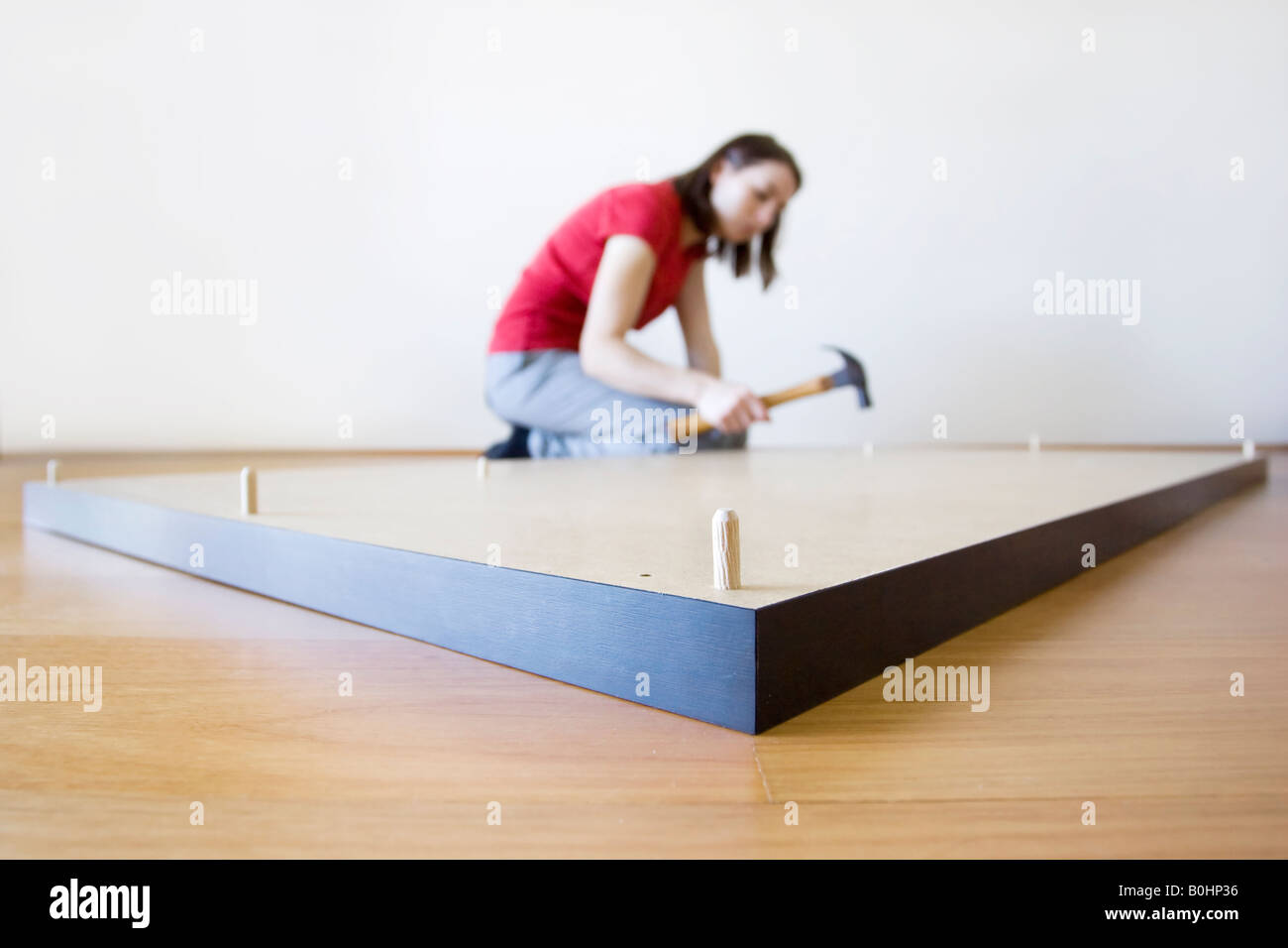 Eine junge Frau klopfen einen Dübel in die Unterseite einer Wohnung packen Selbstmontage Schreibtisch. Stockfoto