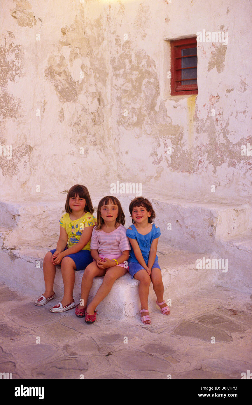 Drei junge Mädchen sitzen durch eine weiß getünchte Wand Mykonos Griechenland Stockfoto