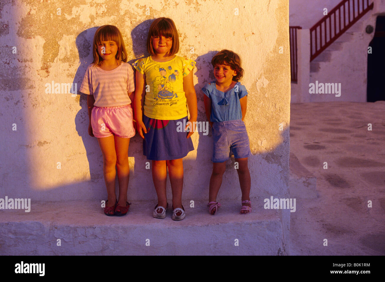 Drei junge Mädchen lehnte sich gegen eine Wand bei Sonnenuntergang Mykonos Griechenland Stockfoto