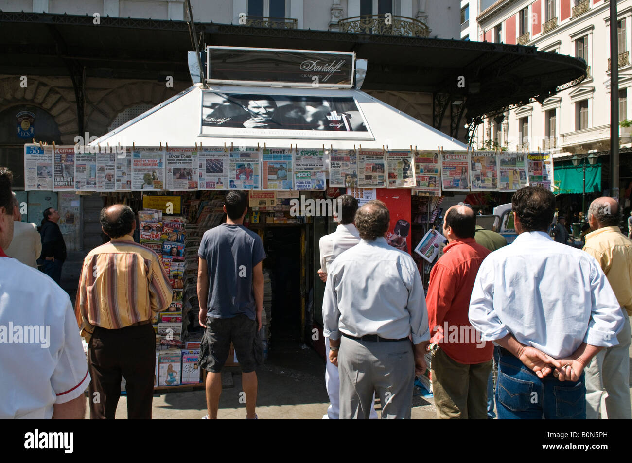 Leute lesen die Schlagzeilen auf Zeitungen oberhalb einer Periptero News-Kiosk in Omonia-Platz, Athen, Griechenland Stockfoto