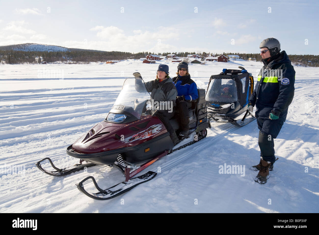 Zwei Frauen in ihre vierziger mit dem Lynx Motorschlitten zu sitzen, während ein Mann in seinen vierziger neben ihnen in Lappland steht / Schweden Stockfoto
