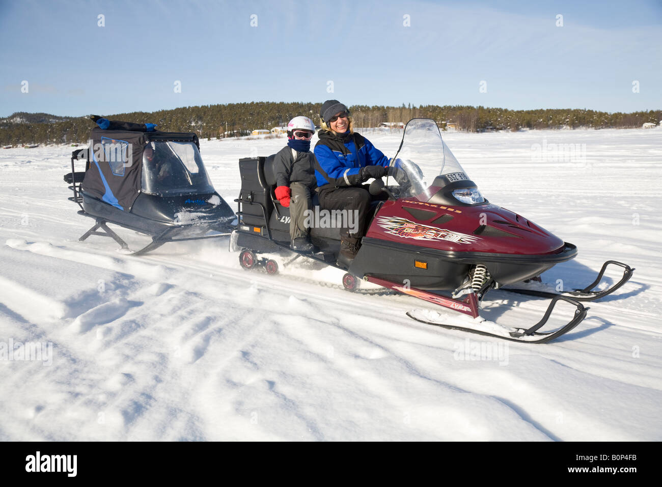 Eine Frau in ihre vierziger-Fahrten ist Lynx Motorschlitten in verschneiten Lappland, ein sechs Jahre altes Mädchen auf dem Rücksitz sitzen. Stockfoto