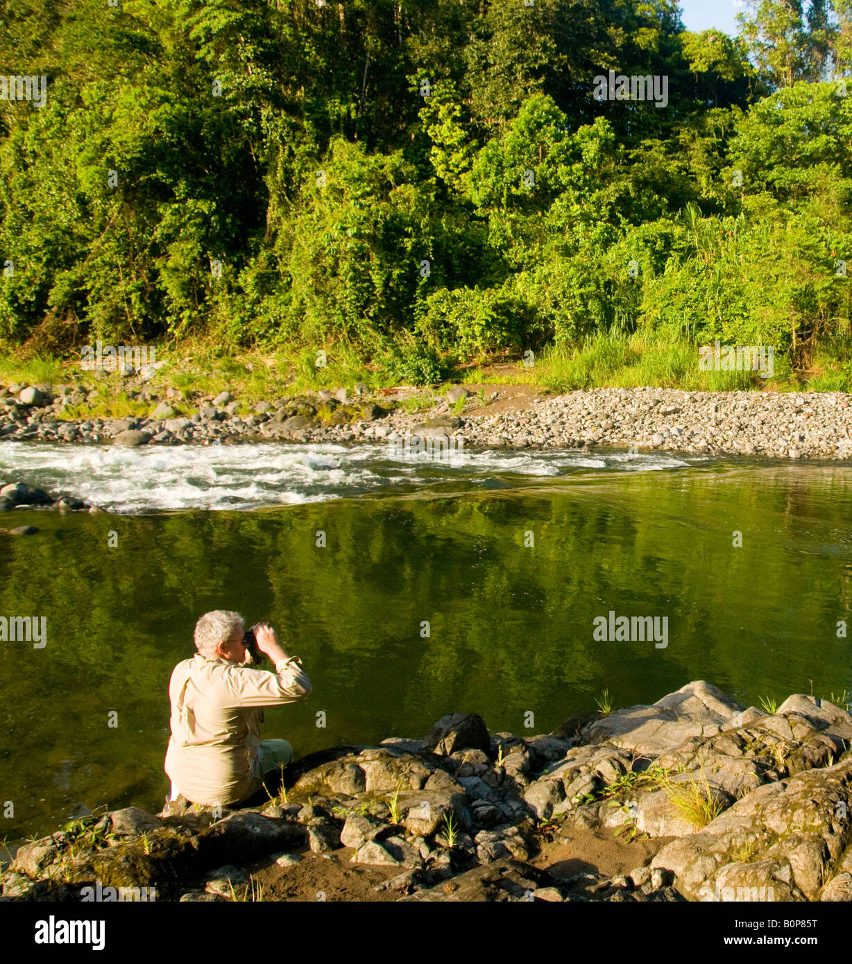 COSTA RICA reifer Mann sitzt auf Flüssen Kante mit dem Fernglas beobachten für Wildtiere Stockfoto