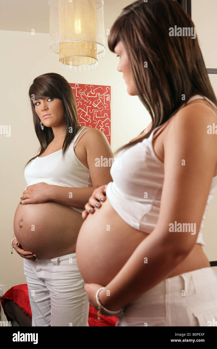 36 Woche spiegeln Teenager Schwangere ihren Bauch halten und schauen sich in ihrem Schlafzimmer Stockfoto