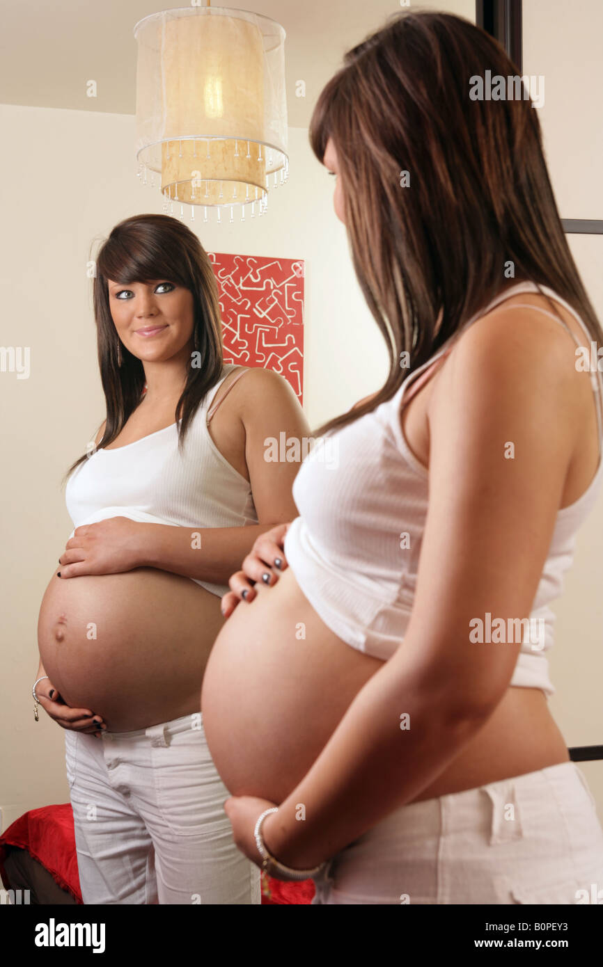 36 Woche spiegeln Teenager Schwangere ihren Bauch halten und schauen sich in ihrem Schlafzimmer Stockfoto