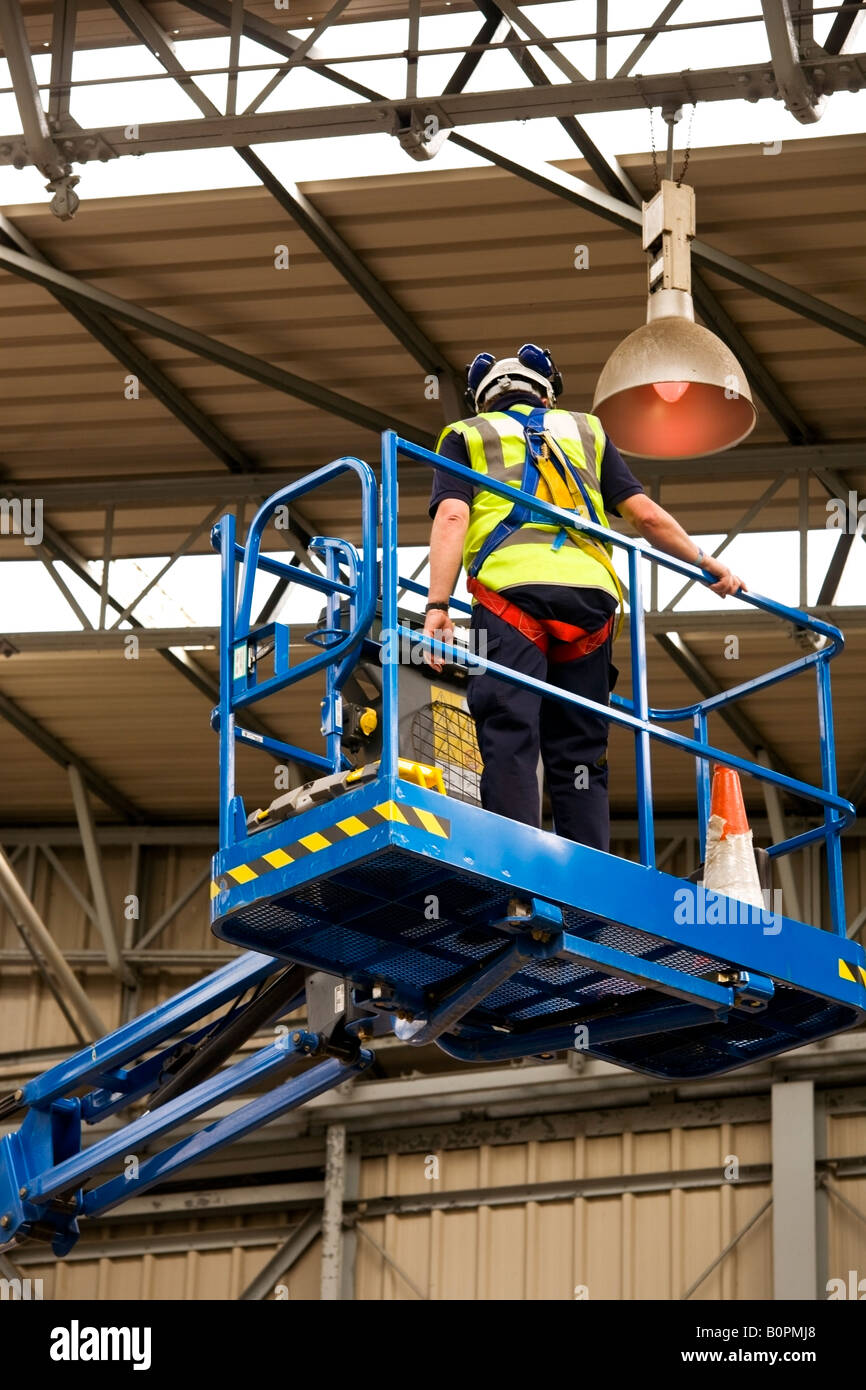 Ein Elektriker, der in der Höhe in einem Hangar auf einem hydraulischen Plattformlift arbeitet Stockfoto