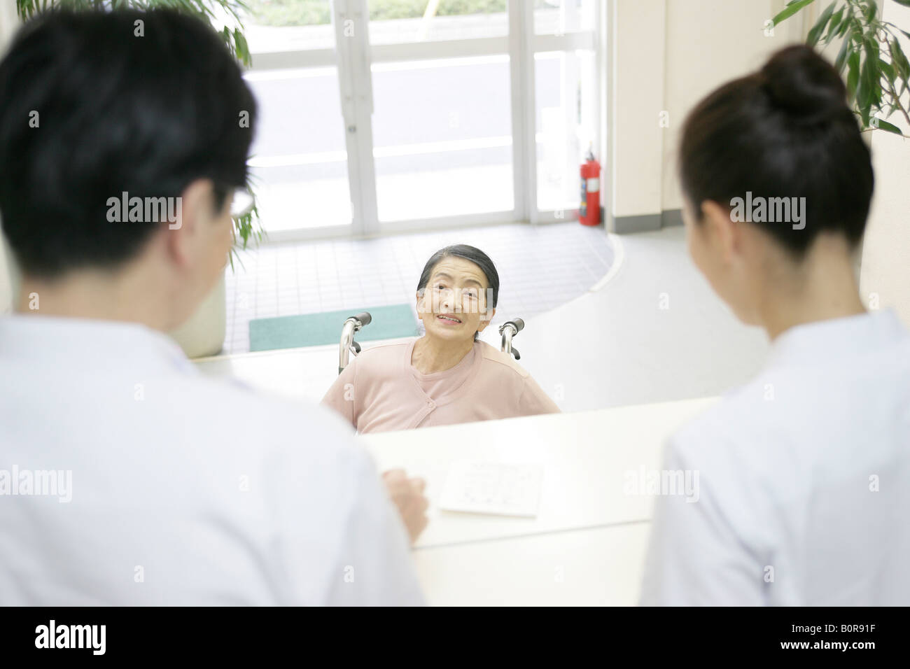 Ältere Frau im Rollstuhl im Gespräch mit Krankenschwestern am Krankenhaus-Schalter Stockfoto