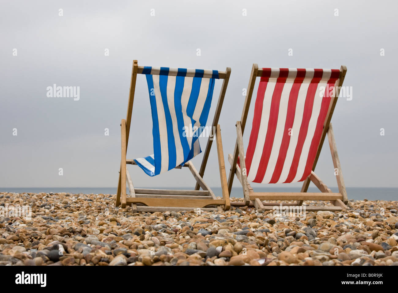 Rote und blaue Liegestuhl liegen leere an einem britischen Strand an einem windigen Tag außerhalb der Saison in den Sommerferien Stockfoto