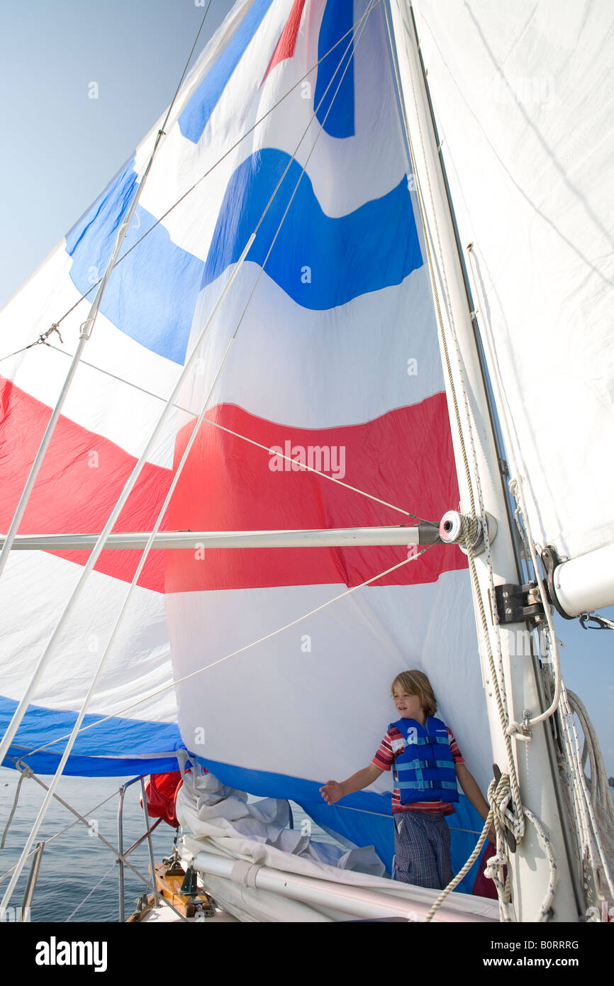 8 Jahre alter Junge mit roten, weißen und blauen Spinnaker Segelboot Segelyacht wind Stockfoto