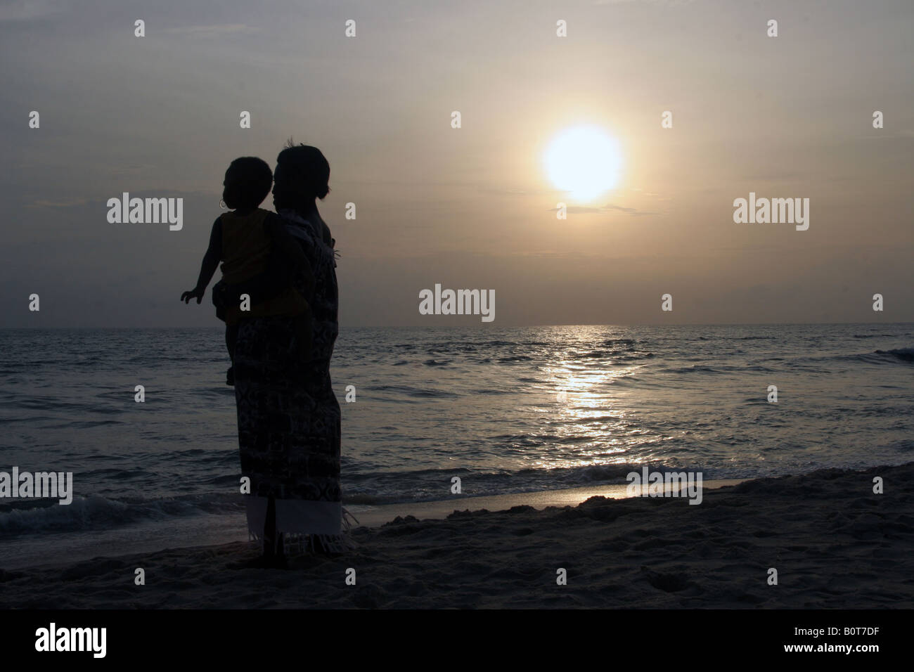 Frau mit Kind starrte auf das Meer bei Sonnenuntergang Stockfoto