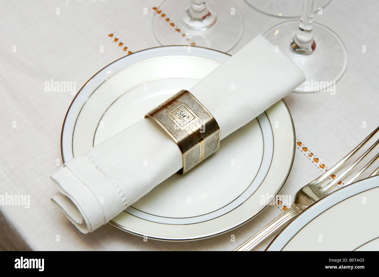 Serviette aus weißer Baumwolle mit silbernem monogrammtem Serviettenring auf Beilagenteller für das Abendessen. Stockfoto