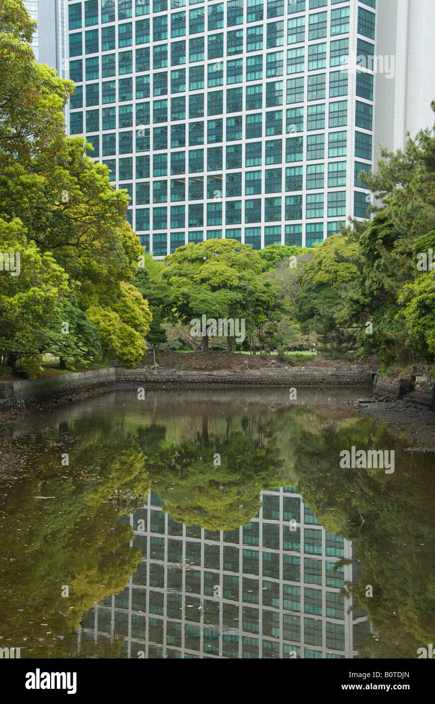 Die grünen getönten Scheiben des Conrad Hotels spiegeln in einen Gezeiten-Kanal an Hamarikyu Gärten. Stockfoto